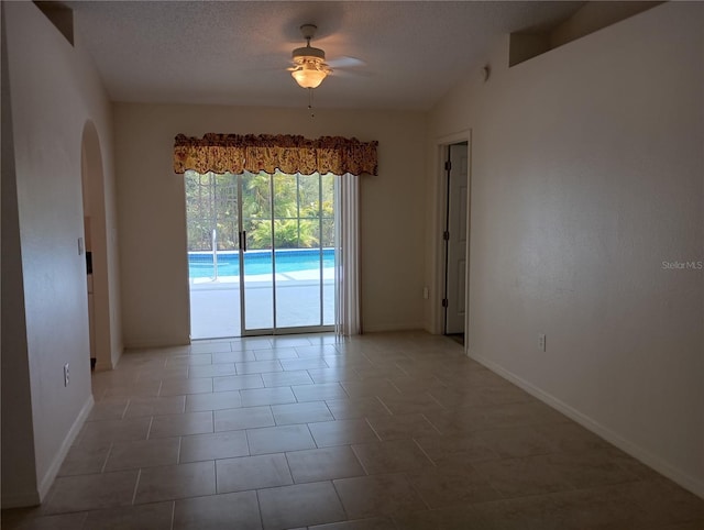 empty room with a textured ceiling, ceiling fan, arched walkways, baseboards, and tile patterned flooring