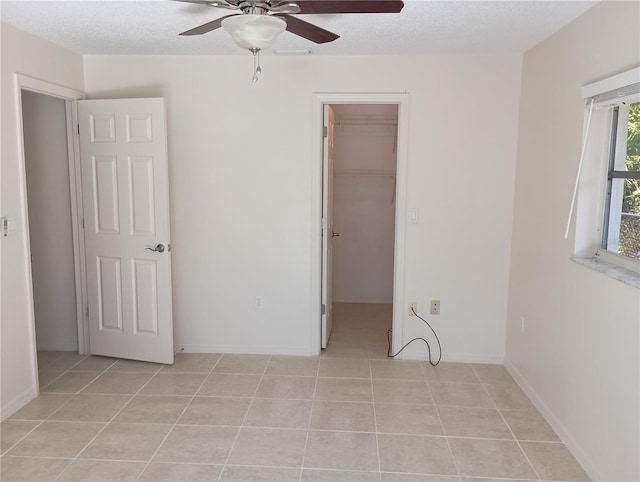 unfurnished bedroom with a spacious closet, light tile patterned floors, a closet, baseboards, and ceiling fan