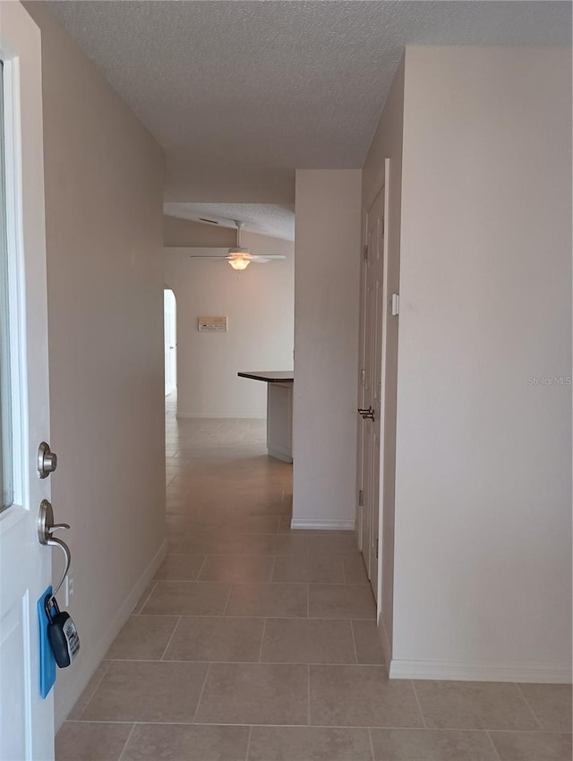 corridor with arched walkways, baseboards, a textured ceiling, and light tile patterned floors