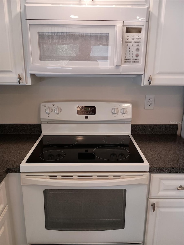 details with white cabinetry, dark countertops, and white appliances