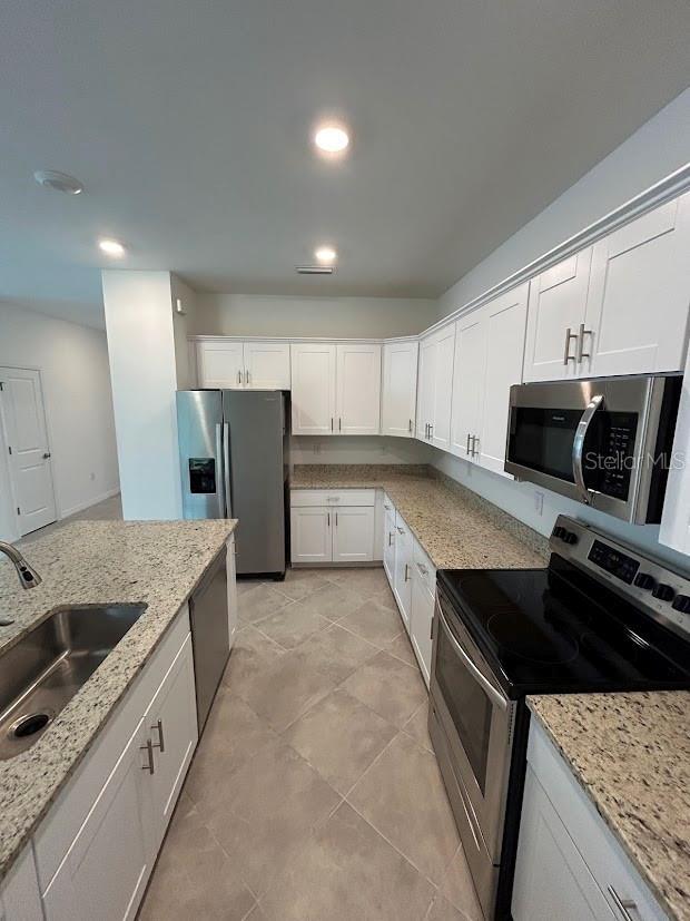 15968 Honeysuckle St, Port Charlotte, FL 33953 - kitchen with appliances with stainless steel finishes, a sink, white cabinets, light stone countertops, and recessed lighting