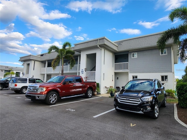 multi unit property with stucco siding, uncovered parking, mansard roof, and roof with shingles
