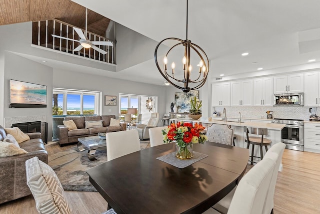 17 Seawatch Dr, Boca Grande, FL 33921 - dining space featuring ceiling fan with notable chandelier, light wood-style floors, a fireplace, a high ceiling, and recessed lighting