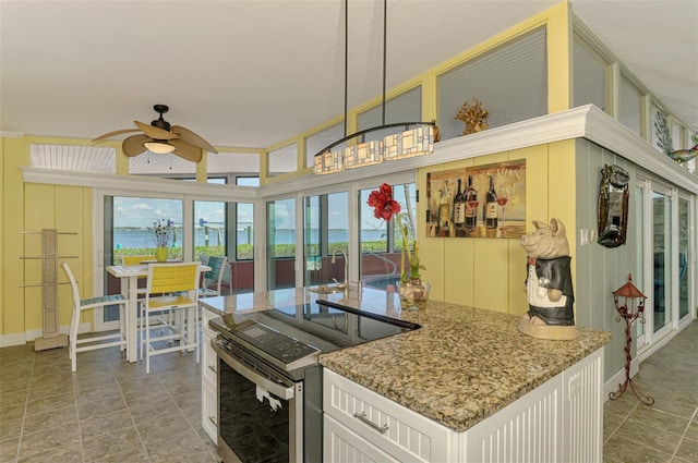 interior space featuring ceiling fan, a wealth of natural light, light stone counters, and stainless steel electric range oven