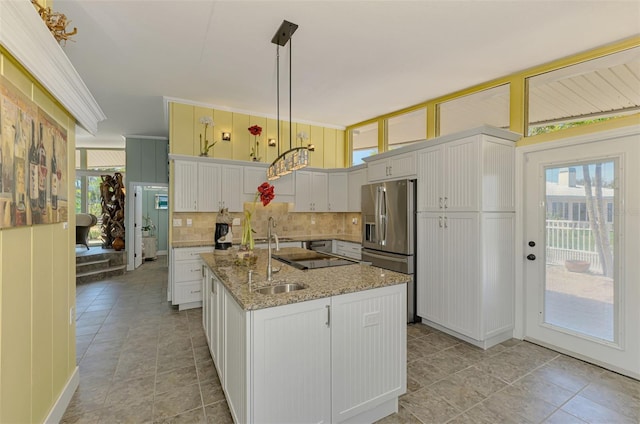 kitchen with light stone counters, a sink, an island with sink, backsplash, and stainless steel refrigerator with ice dispenser