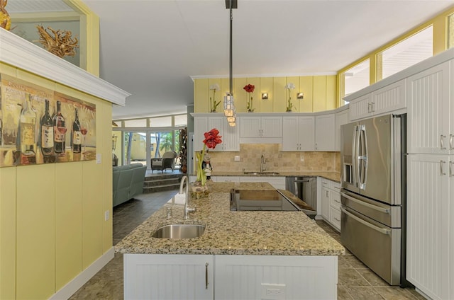 kitchen with decorative backsplash, stainless steel fridge with ice dispenser, a sink, and a center island with sink