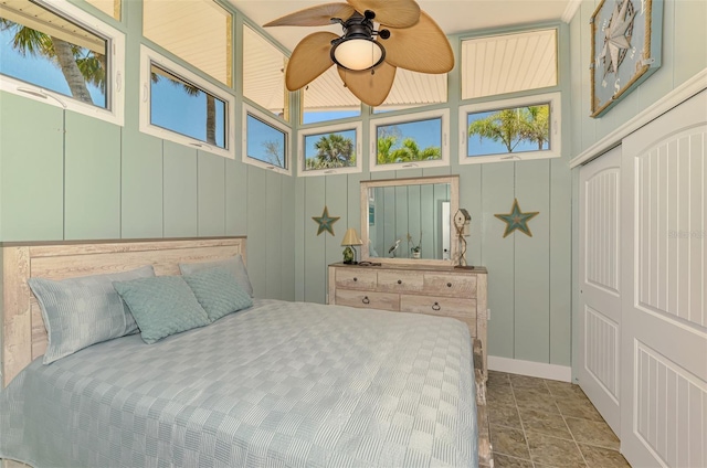bedroom with a decorative wall, a closet, stone finish floor, and baseboards