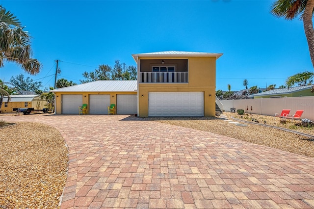 view of front facade with fence, a balcony, stucco siding, ceiling fan, and metal roof