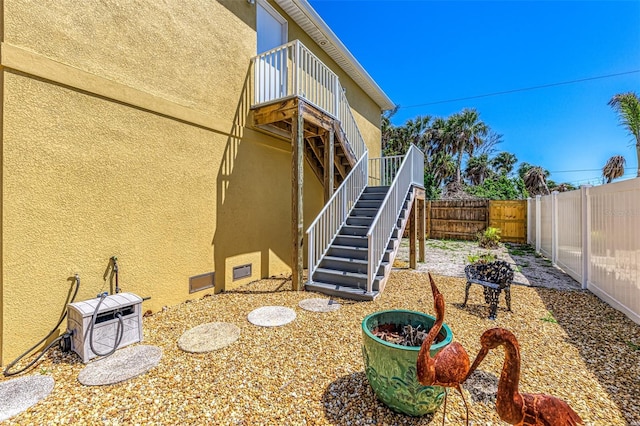 back of house with stairway, a balcony, a fenced backyard, ac unit, and stucco siding