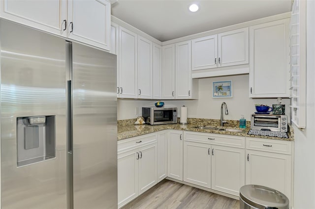 kitchen with a sink, light wood-style floors, white cabinetry, appliances with stainless steel finishes, and light stone countertops