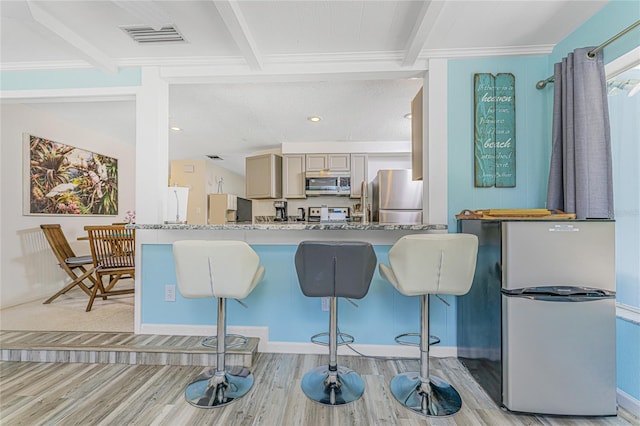 kitchen featuring a kitchen breakfast bar, visible vents, beam ceiling, stainless steel appliances, and light wood finished floors