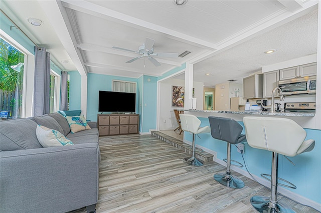 living area featuring visible vents, beamed ceiling, a ceiling fan, and light wood-style floors