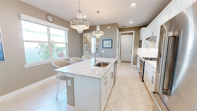 kitchen with white cabinetry, under cabinet range hood, a kitchen island with sink, a sink, and high quality appliances