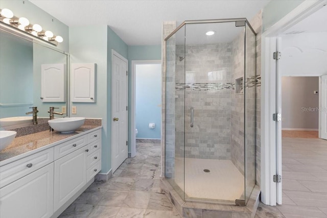 bathroom featuring a shower stall, toilet, a sink, double vanity, and baseboards