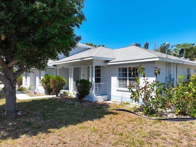 view of front of house with a porch, a front lawn, stucco siding, and a shingled roof