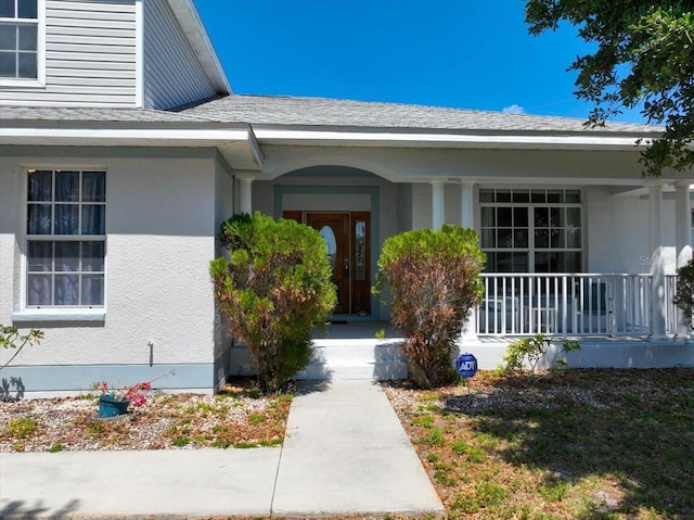 view of exterior entry with a porch, stucco siding, and a shingled roof