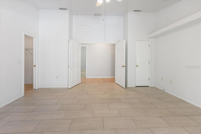 unfurnished room featuring a ceiling fan, a towering ceiling, visible vents, and light wood-type flooring