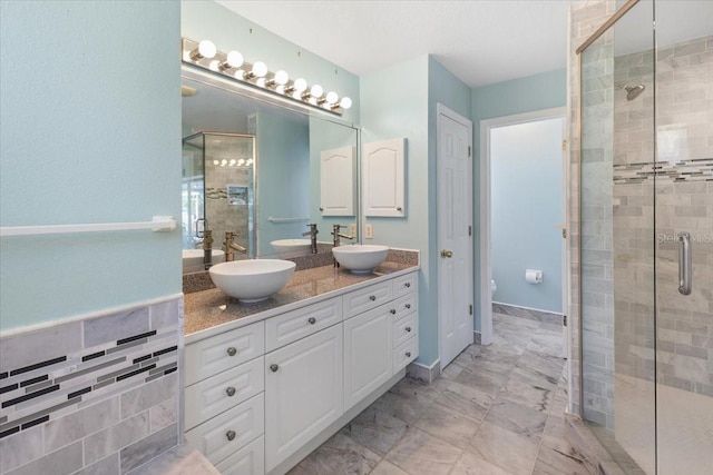 full bath with marble finish floor, a sink, a shower stall, and double vanity