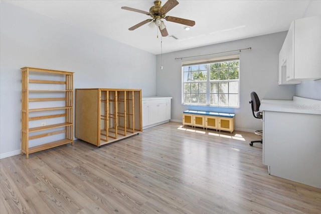 unfurnished office with built in study area, ceiling fan, baseboards, and light wood-style flooring