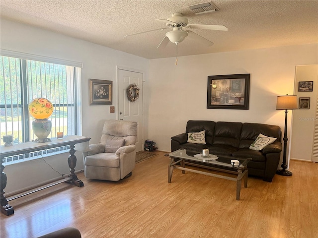 living area featuring light wood-style floors, visible vents, a ceiling fan, and a textured ceiling