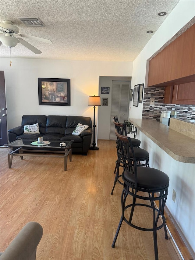 living area with a textured ceiling, ceiling fan, light wood finished floors, and visible vents