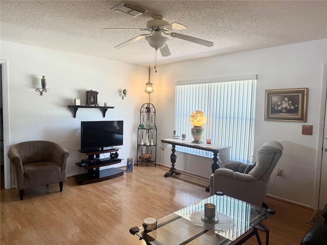 living room with a ceiling fan, visible vents, wood finished floors, and a textured ceiling
