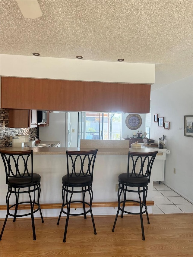 kitchen with a breakfast bar area, a textured ceiling, and brown cabinets