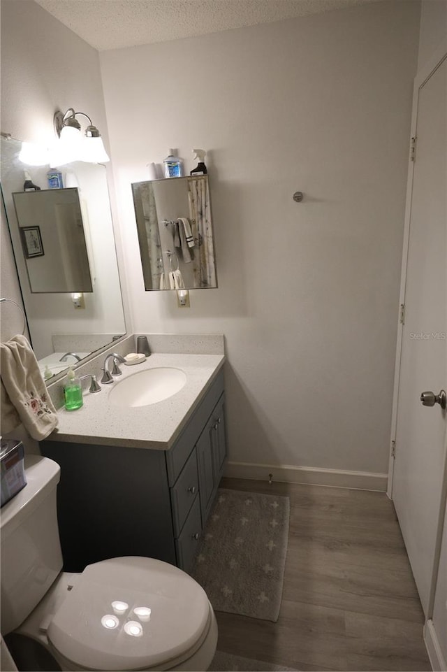 half bathroom featuring wood finished floors, toilet, vanity, and baseboards