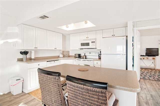 kitchen featuring visible vents, light wood-style flooring, white appliances, and a kitchen bar