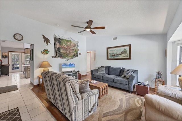 living room with a ceiling fan, a textured ceiling, light tile patterned flooring, and visible vents