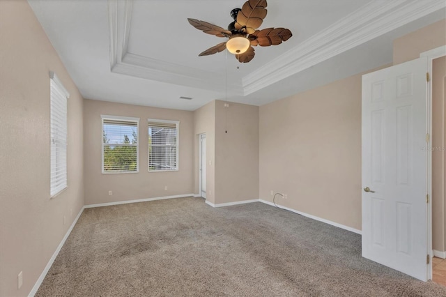 spare room with a tray ceiling, baseboards, carpet floors, ornamental molding, and a ceiling fan