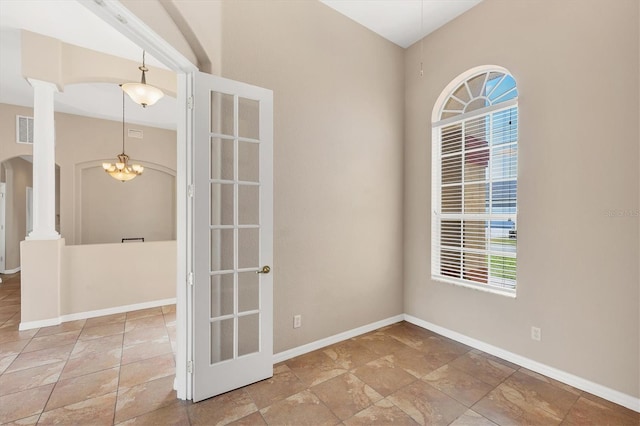 spare room featuring stone tile floors, baseboards, arched walkways, and a chandelier