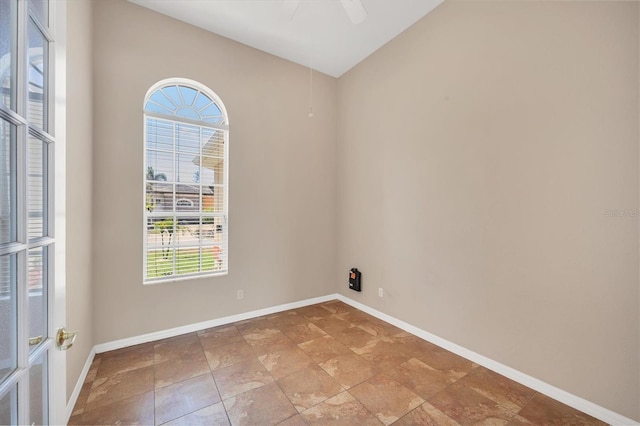 empty room with stone finish flooring, a ceiling fan, vaulted ceiling, and baseboards