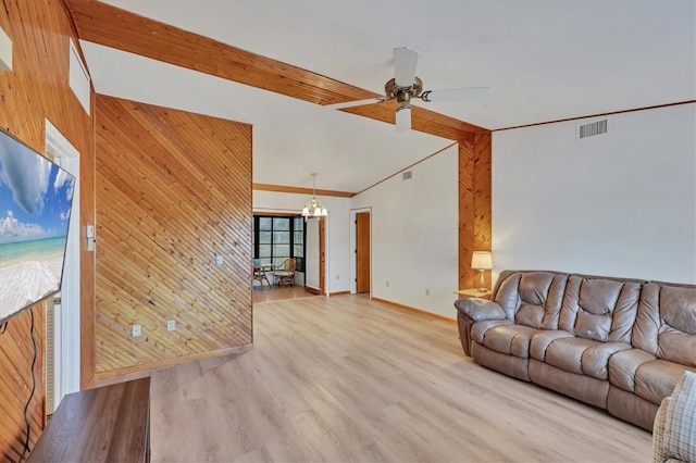 living room with light wood-style floors, wooden walls, visible vents, baseboards, and ceiling fan with notable chandelier