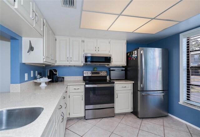 kitchen with light tile patterned floors, stainless steel appliances, light countertops, white cabinetry, and visible vents