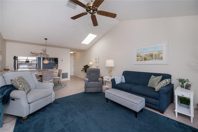 tiled living area with carpet flooring, visible vents, lofted ceiling with skylight, and ceiling fan