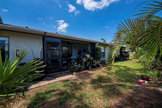 rear view of house with stucco siding, a sunroom, and a yard