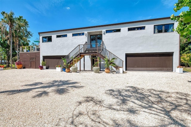 view of front of house featuring stairs, an attached garage, stucco siding, french doors, and driveway
