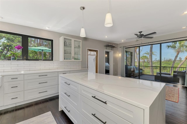 kitchen with a healthy amount of sunlight, light stone countertops, backsplash, and white cabinetry