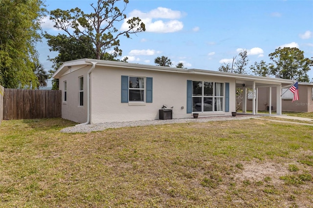 view of front of house with central air condition unit, a front lawn, a carport, fence, and stucco siding