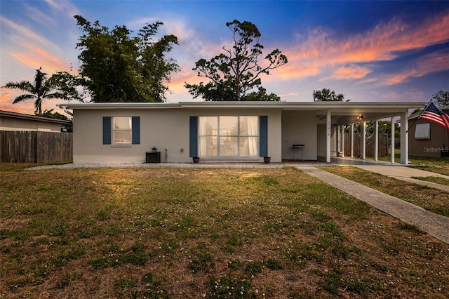 back of property at dusk with stucco siding, fence, an attached carport, and a lawn