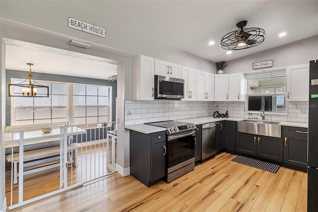 kitchen featuring light wood-style flooring, a sink, backsplash, light countertops, and appliances with stainless steel finishes