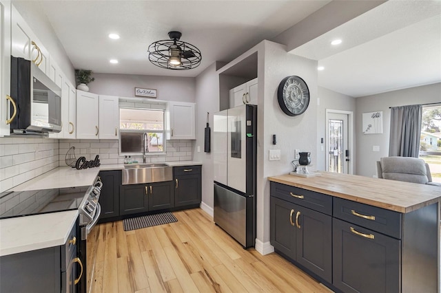 kitchen with a sink, butcher block counters, stainless steel appliances, backsplash, and white cabinetry