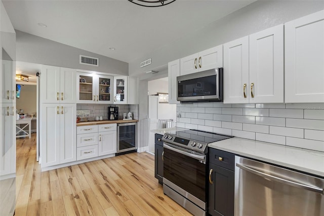 kitchen featuring beverage cooler, stainless steel appliances, lofted ceiling, white cabinetry, and visible vents