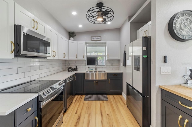 kitchen featuring stainless steel appliances, backsplash, a sink, light wood-style floors, and white cabinetry