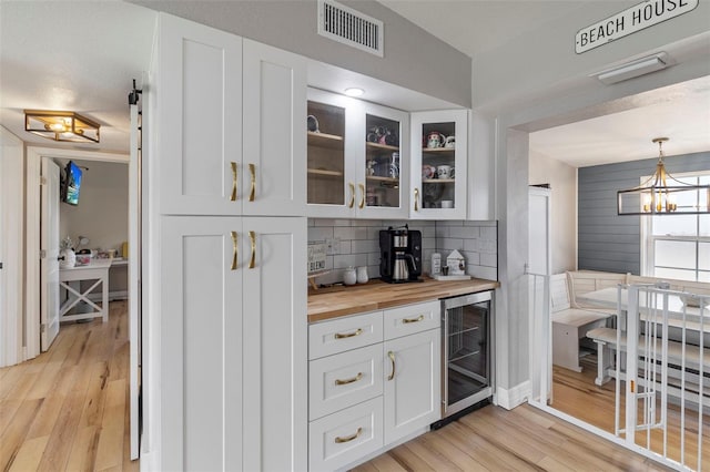bar featuring light wood finished floors, wine cooler, visible vents, and tasteful backsplash