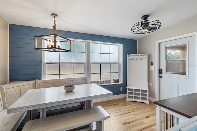 dining room with baseboards, wood walls, light wood-style floors, and ceiling fan with notable chandelier