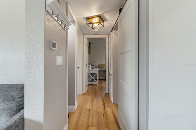corridor with a textured wall, light wood-style flooring, and baseboards