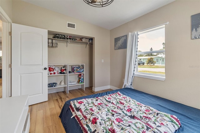bedroom featuring baseboards, wood finished floors, visible vents, and a closet