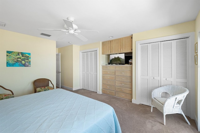 bedroom featuring carpet, visible vents, baseboards, two closets, and ceiling fan